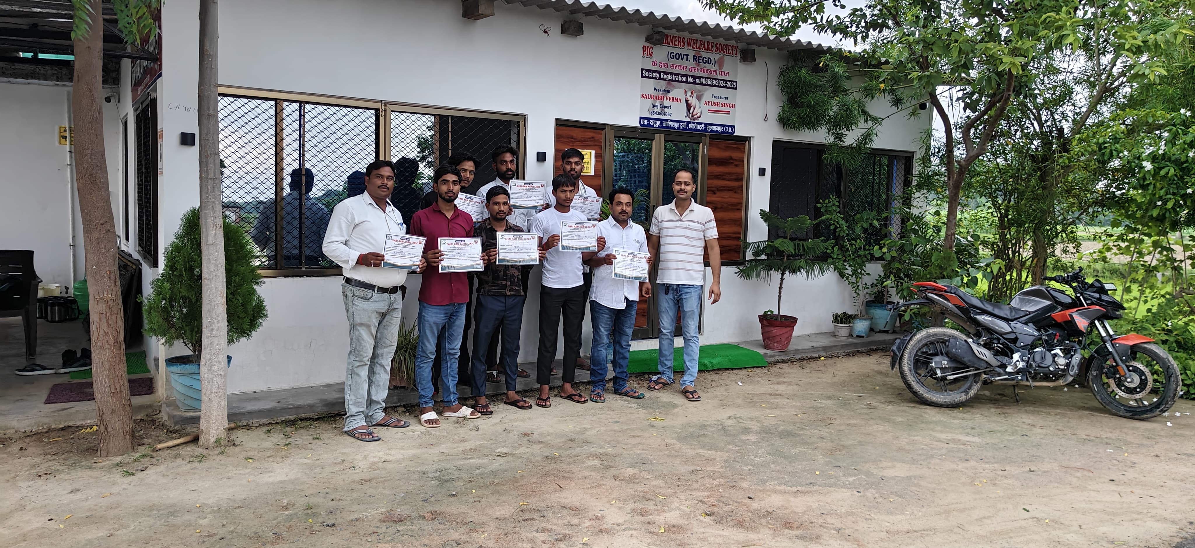 केंद्र के बाहर अपने आधिकारिक प्रमाण पत्र लिए हुए सुअर पालन प्रशिक्षुओं के साथ समूह बाहरी फोटो सत्र